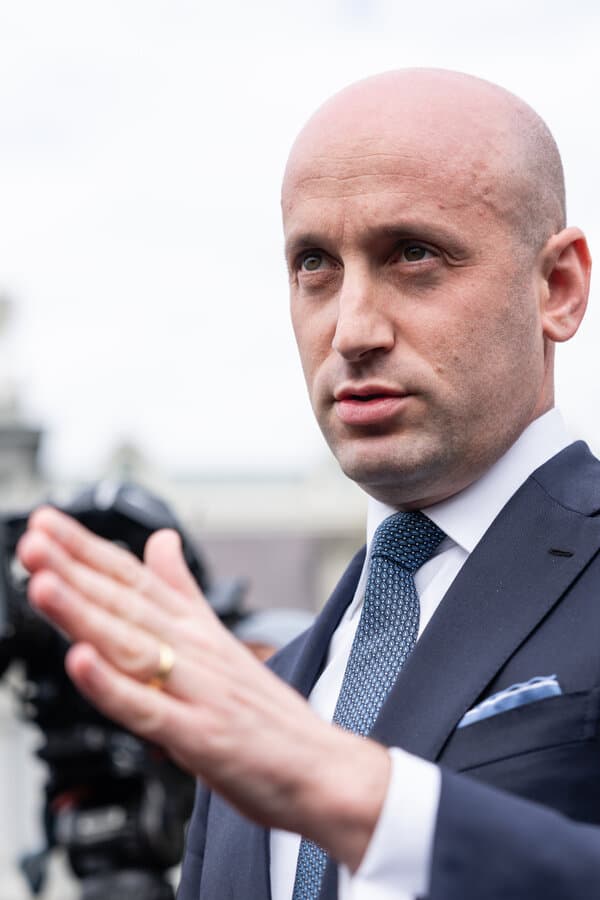 Stephen Miller speaking at a podium with American flag background