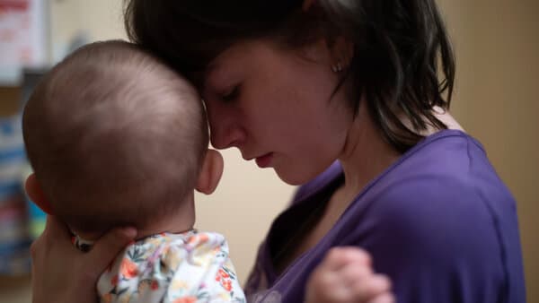A still from the documentary 'Young Mothers' showing a teenage girl looking down at her baby.