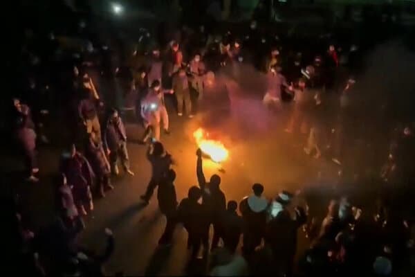 Protesters clashing with security forces on a street in Iran at night.