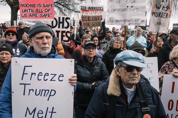 A crowd of protesters gathered on a city street holding signs regarding ICE and immigration.
